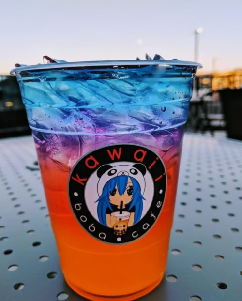 A colorful layered drink in a clear cup from Kawaii Boba Cafe, featuring ice and a vibrant blue to orange gradient.